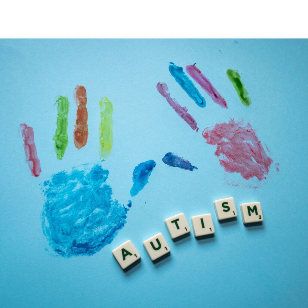 zwei bunte Hände auf blauem Untergrund mit einzelnen Scrabble-Steinen, die zu dem Wort Autism zusammen gefügt wurden